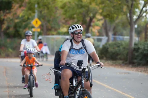 A family rides bikes together down a tree-lined path in the distance.