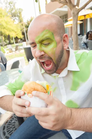 A man in green zombie face paint opens his mouth in a mock roar.