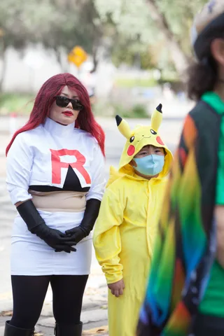A woman dressed as Team Rocket stands with a child in a Pikachu costume and mask.