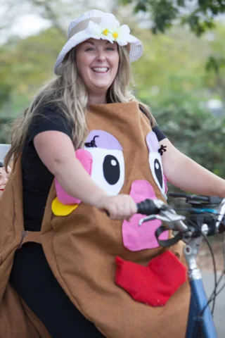 A close view of a plush animal-face costume seen from behind on a bike.