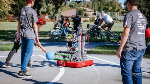 A man tosses a ball to a small wheeled robot on a park path.