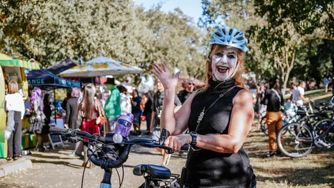 A woman in a helmet waves cheerfully near the vendor booths.
