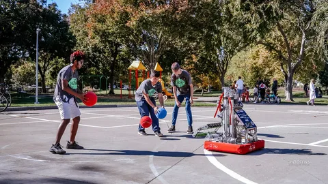 Teens operate a small robot on the court while others watch.