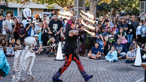 A fire performer swings blazing fans in front of a huge attentive downtown crowd.