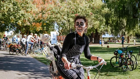 A woman in skeleton face makeup smiles while sitting on her bike.