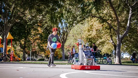 A boy tosses a ball toward a small competition robot.