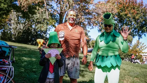 A man in an orange dinosaur costume and a man in a green leaf costume pose together.
