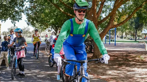 A man in a green Luigi costume sits on his bike with other riders behind him.