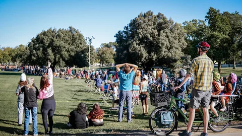 A large crowd gathers on the grass, hands raised toward the sky.
