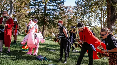Costumed musicians play saxophones beside a giant inflatable pink dinosaur.