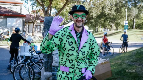 A man in a green Riddler suit and bowler hat waves in front of the Davis Arts Center.