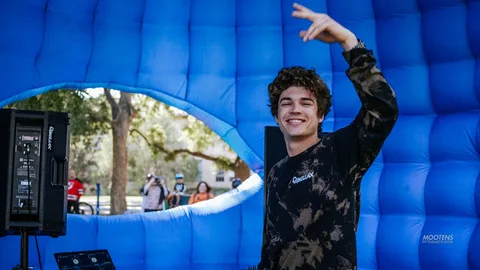 A teen gestures inside a glowing blue inflatable tunnel at a DJ booth.