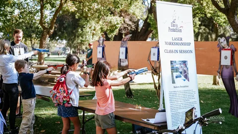 Kids aim laser pistols at a shooting-range booth beside a Davis Pentathlon banner.