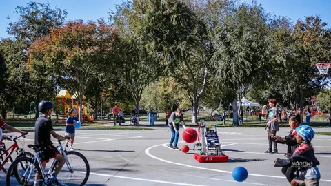 A wide view of the park basketball court with people scattered around.