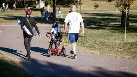 Two people walk together with an adaptive trike along the path.