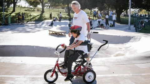 Two riders on red adaptive trikes sit together at the skate park.