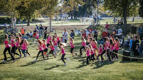 A youth dance team in pink tank tops runs across the grass mid-performance.