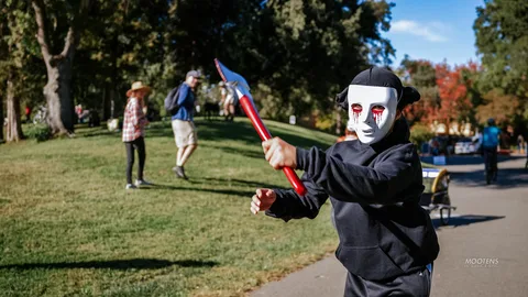 Two white-faced performers in black costumes mock-duel with a glowing red sword.
