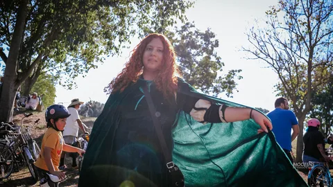A woman in a dramatic green cape strikes a pose in the park.