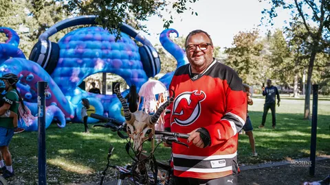 A man in a hockey jersey poses beside a skull-topped Halloween display.