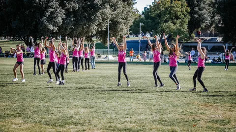 A youth dance team strikes a pose with arms raised on the open field.