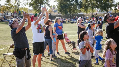 A family looks up together, arms raised, a child in a superhero shirt among them.