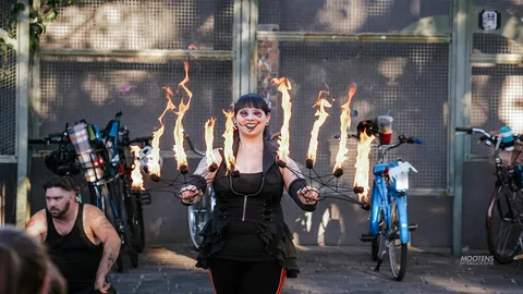 A fire performer in devil-horn makeup smiles with blazing claw fans spread wide.