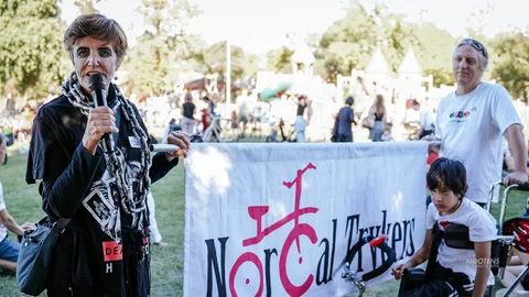 A speaker addresses the crowd on a microphone beside the NorCal Trykers banner.