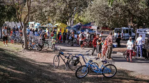 Festival-goers with bikes gather along the shaded vendor path.