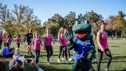 The dance team performs near the frog mascot and a small crowd.