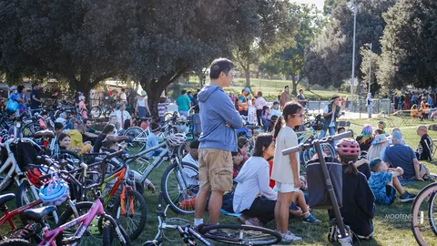 Festival-goers and cyclists gather near a roped-off area in the park.