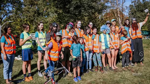 A line of volunteers in orange safety vests poses together for a group photo.