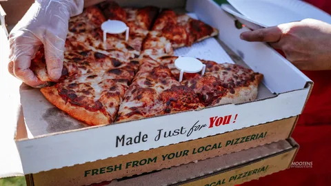 A hand holds up a slice of pizza from a local pizza box.