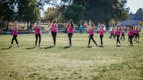 A youth dance team raises their arms mid-routine on the grass.