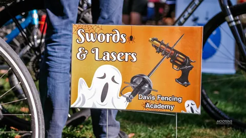 A Swords and Lasers sign advertises the Davis Fencing Academy booth.