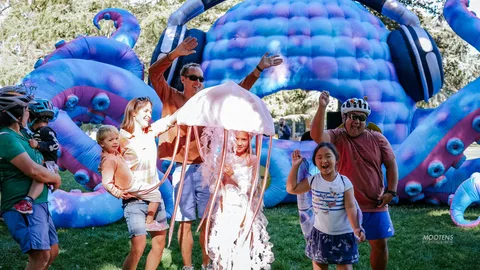 A family raises their arms in celebration beneath a giant inflatable jellyfish.