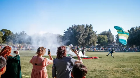 Costumed spectators watch and photograph the finale with smoke drifting behind them.