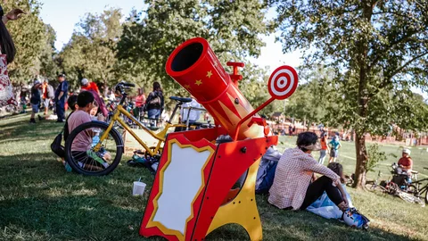 A red carnival cannon-and-target game stands under the trees.