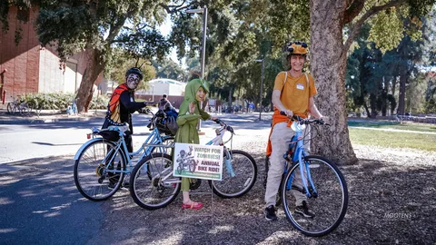 Three riders pause with their bikes on a park road.