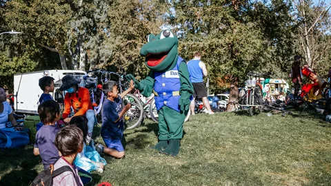 A green frog mascot in a Davis vest greets children at the festival.