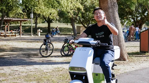 A man gives a thumbs up while riding an electric bike through the park.