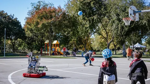 A wide view of the park with families scattered near a playground and basketball court.