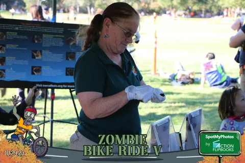 A volunteer at an information booth handles paperwork with gloved hands.