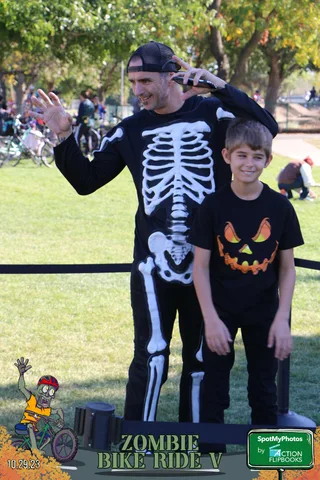 A boy in a skeleton-themed shirt smiles as an adult's arm reaches into frame.
