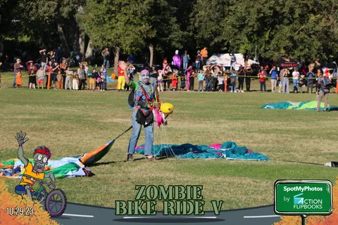 A skydiver stands on the grass beside a collapsed parachute.