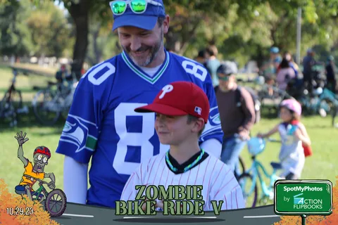 A man and a boy in sports jerseys pose together with the festival crowd behind them.