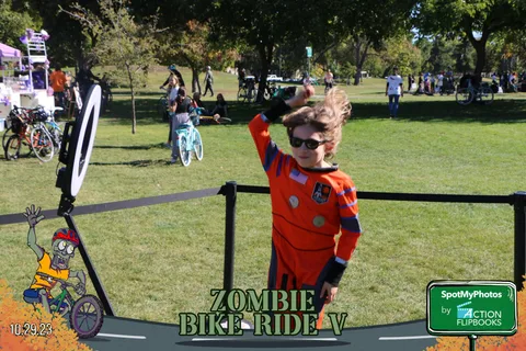 A boy in a costume and bike helmet jumps and waves for the camera.