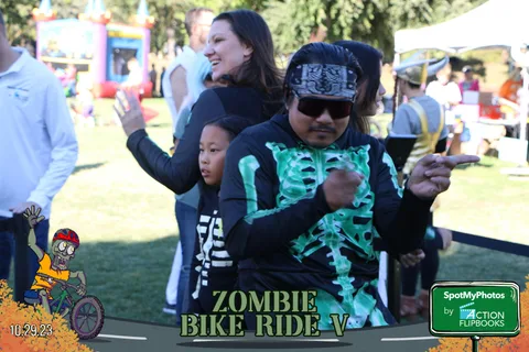 A man poses with a girl in a skeleton costume, both with arms out.