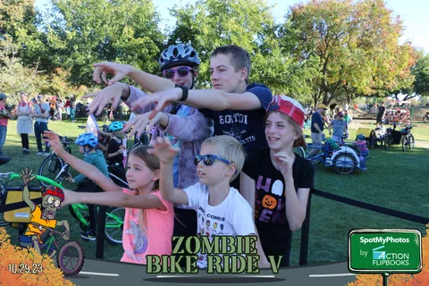 A group of kids and teens make playful zombie gestures behind a barrier.