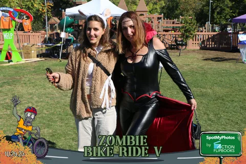 Two women in fur coat and black catsuit costumes pose together.